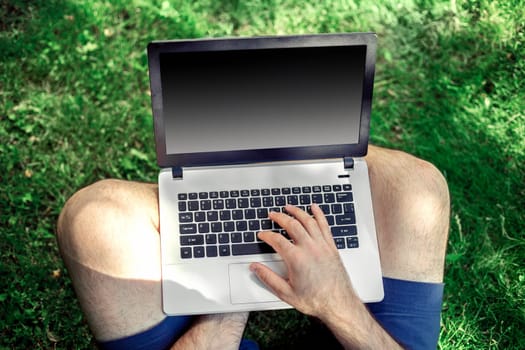 Young blogger sitting on grass and working with laptop. Copy space