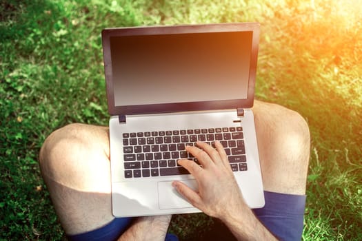 Young blogger sitting on grass and working with laptop. Copy space. Sun flare