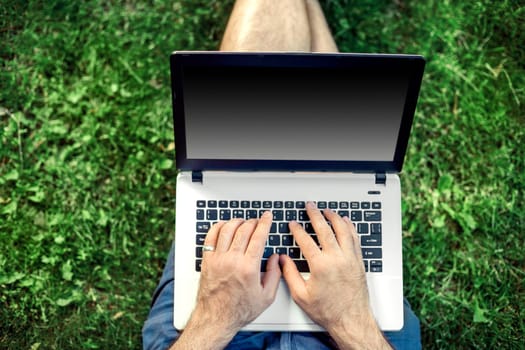 Young blogger sitting on grass and working with laptop. Copy space