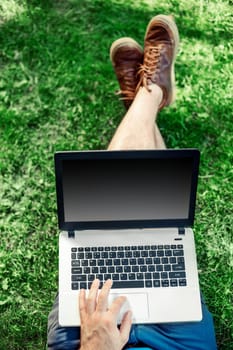 Young blogger sitting on grass and working with laptop. Copy space