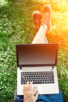 Young blogger sitting on grass and working with laptop. Copy space. Sun flare