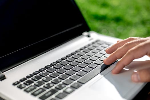 Close-up shot of handsome man's hands touching laptop computer's screen. Businessman using a laptop computer and sitting on the ground.