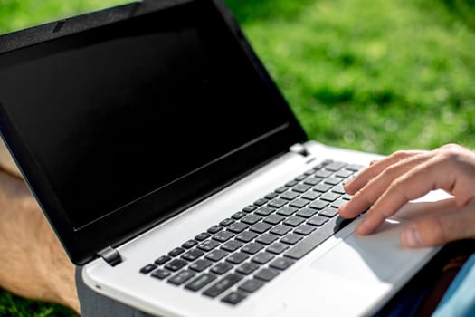 Close-up shot of handsome man's hands touching laptop computer's screen. Businessman using a laptop computer and sitting on the ground.