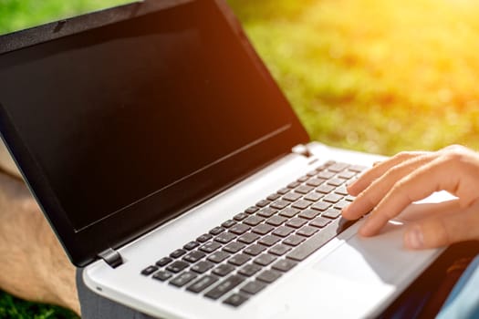 Close-up shot of handsome man's hands touching laptop computer's screen. Businessman using a laptop computer and sitting on the ground.. Sun flare