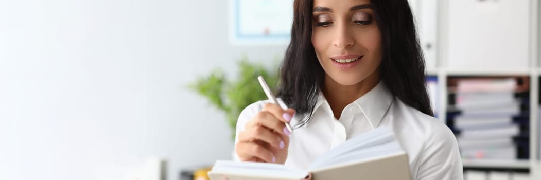 Beautiful woman smiles thoughtfully and holds pen and diary. Weekly planning and business plan