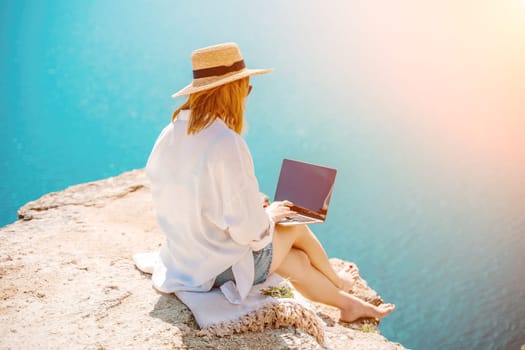 Freelance woman working on a laptop by the sea, typing away on the keyboard while enjoying the beautiful view, highlighting the idea of remote work