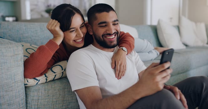 Couple, phone and laughing at meme on social media or internet joke and relax in a living room couch in a home. Sofa, cellphone and people streaming online comedy on a smartphone in a house together.