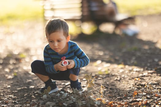 Little boy crouched in the park holding soap bubbles stick. Mid shot