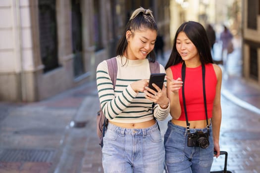 Two young Chinese females passing by guided by the GPS of their smartphone, through the streets of Granada, Spain. Concept of Asian people traveling in Europe.