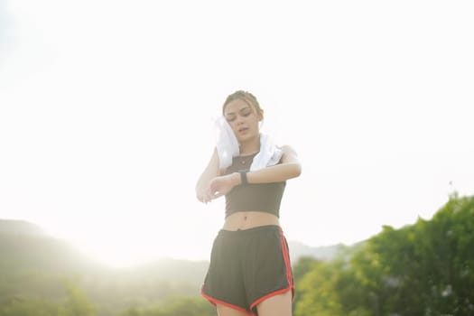 Young woman jogging and looking at her smart wrist watch, copy space, outdoor.