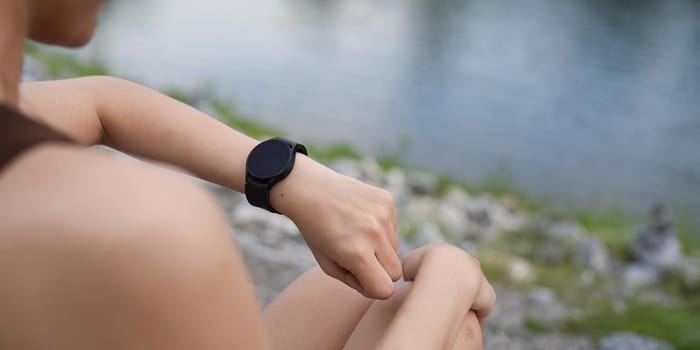 Young woman jogging and looking at her smart wrist watch, copy space, outdoor.
