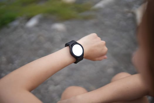 Young woman jogging and looking at her smart wrist watch, copy space, outdoor.