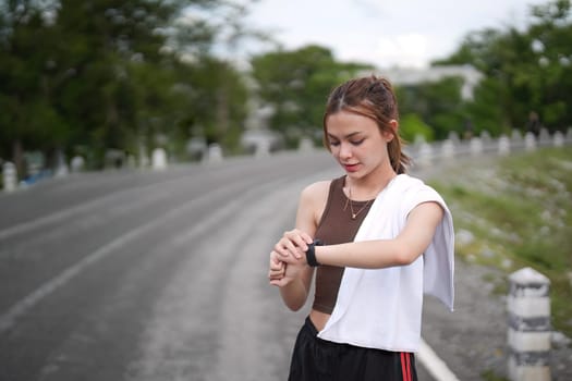 Young woman jogging and looking at her smart wrist watch, copy space, outdoor.