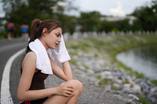 Young woman wiping sweat on face and neck during exercise in the city at sunrise. Young female take a break from training before workout. Healthy and active lifestyle concept.