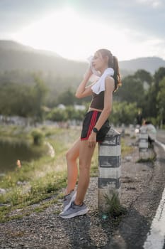 Young woman wiping sweat on face and neck during exercise in the city at sunrise. Young female take a break from training before workout. Healthy and active lifestyle concept.