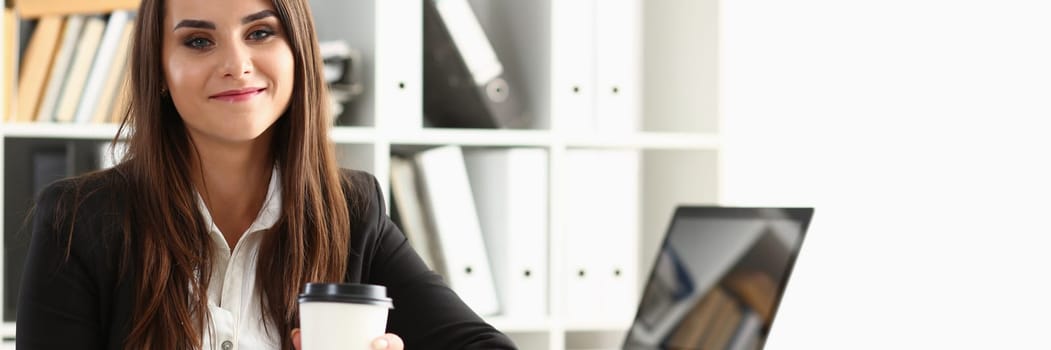 Beautiful young businesswoman holding glass of coffee at workplace. Break and rest in office concept