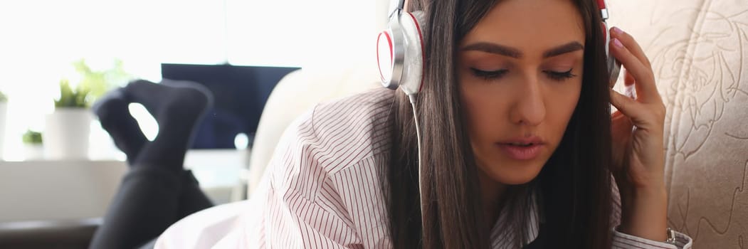 Young woman in headphones is relaxing on sofa and listening to music online using smartphone. Music and educational apps for phone