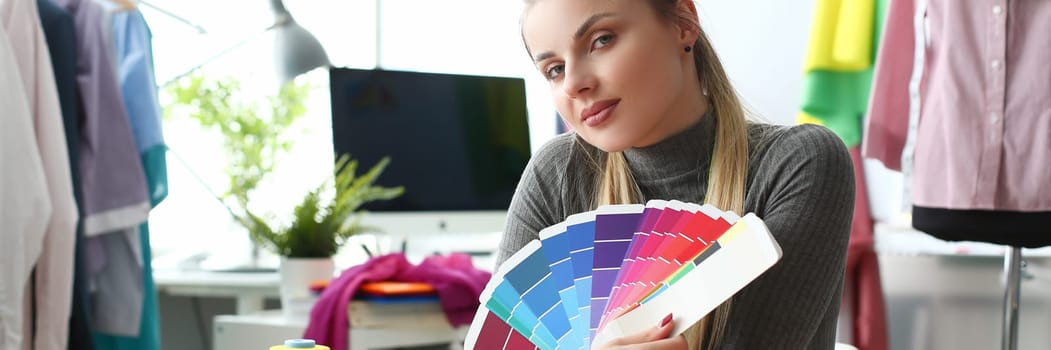 Female fashion designer seamstress working in studio holding color palette. Selection and choice of color solution in concept clothing collection