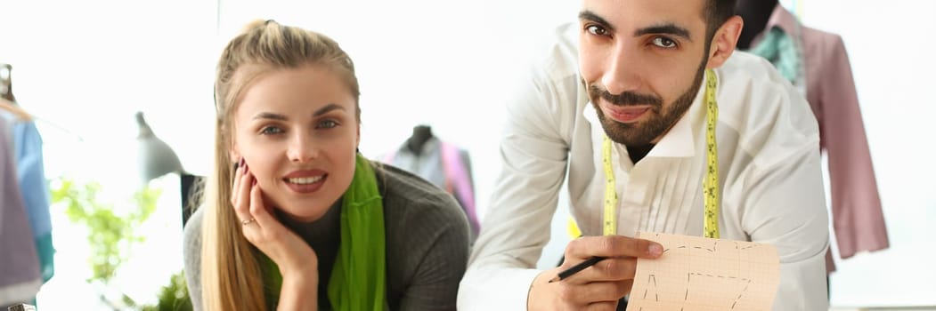 Young business woman stylist seamstress holding tablet male colleague showing sketches of clothes. Discussion of a new collection of clothes in creative sewing workshop