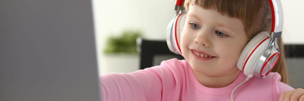 Portrait of a little child girl in headphones with laptop. Watching cartoons and kids remote learning concept