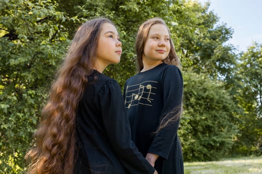 Two Little Girls, Sisters With Extra Long Curly Shiny Hair Hold Hands In Park, Nature On Background. Outdoor, Sunny Day. Cute Happy Kids In Dress Walking In Meadow. Siblings. Horizontal Plane.