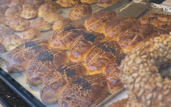 Many different pastries lie behind a glass window of a bakery shop.