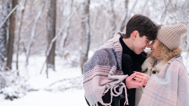 A young couple walks in the park in winter. The guy and the girl are drinking a warming drink outdoors