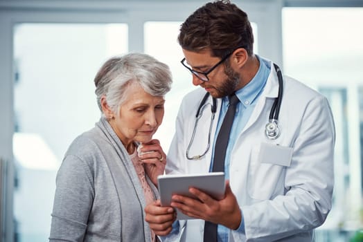 Ensuring his patient understands every detail of the treatment procedure. a doctor discussing something on a digital tablet with a senior patient in a clinic