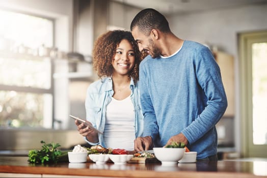 Shot of a happy young couple using a digital tablet while preparing a healthy meal together at home.