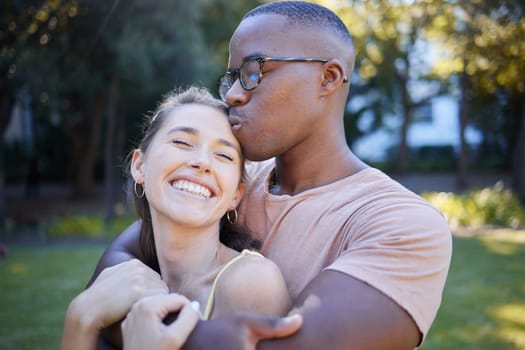 Interracial, couple hug and kiss in park, date outdoor in nature, happiness with love and commitment in relationship. Trust, support and happy woman with smile, black man content with fresh air.