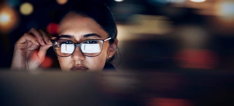 Woman, glasses reflection and computer at night for planning, website search and technology. Face of female working late on desktop, dark office and reading online network, focus vision and internet.