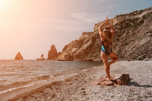 Woman sea yoga. Back view of free calm happy satisfied woman with long hair standing on top rock with yoga position against of sky by the sea. Healthy lifestyle outdoors in nature, fitness concept.