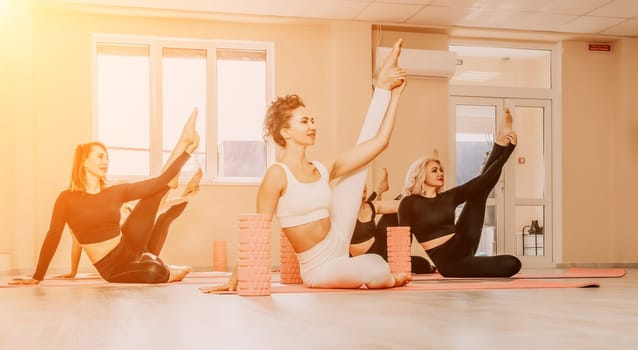 Group of young womans fitness instructor in Sportswear Leggings and Tops, stretching in the gym before pilates, on a yoga mat near the large window on a sunny day, female fitness yoga routine concept.