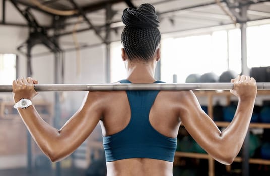 Fitness, black woman or bodybuilder with a barbell in training, workout or exercise for body goals. Back view, mindset or sports athlete weightlifting with strong biceps or focus at gym club studio.