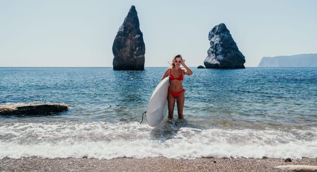 Close up shot of beautiful young caucasian woman with black hair and freckles looking at camera and smiling. Cute woman portrait in a pink bikini posing on a volcanic rock high above the sea