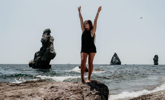 Woman travel sea. Young Happy woman in a long red dress posing on a beach near the sea on background of volcanic rocks, like in Iceland, sharing travel adventure journey