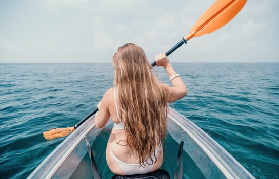 Woman in kayak back view. Happy young woman with long hair floating in transparent kayak on the crystal clear sea. Summer holiday vacation and cheerful female people having fun on the boat.