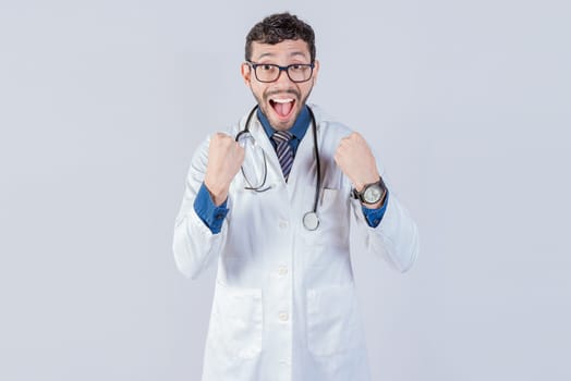 Young doctor is happy celebrating something, he is wearing glasses and stethoscope, he is looking at the camera with amazed face