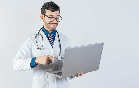 Young doctor in glasses using notebook on isolated background. Handsome doctor using laptop isolated. Smiling doctor standing using laptop isolated