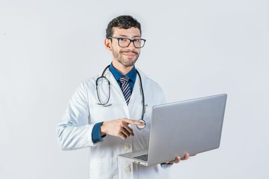 Smiling doctor using and pointing laptop isolated. Young doctor in glasses using laptop and looking at camera. Handsome doctor using laptop isolated