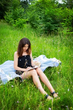 Outdoor picnic. A girl reads a book in the open air while sitting on a blue plaid. The girl enjoys the fresh air. Outdoor recreation, close-up