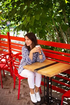 Portrait of a young beautiful woman sitting in an outdoor cafe on an open beautiful terrace drinking coffee