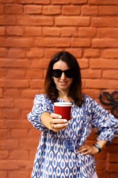 Portrait of a young beautiful woman holding a plastic red glass with coffee in front of her