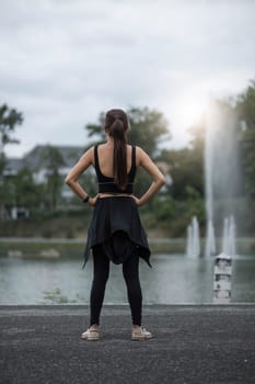 A portrait of a sporty and happy young Asian woman in sportswear is stretching her arms, warming up her body before running outdoors. Outdoor activity concept..