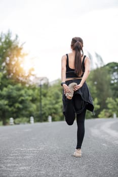 Back view, A sporty Asian woman in sportswear is stretching her body and warming up before running on the street in the park...