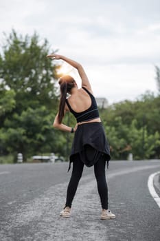 Back view, A sporty Asian woman in sportswear is stretching her body and warming up before running on the street in the park...