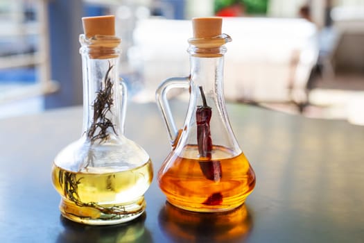 On the table are two glass bottles filled with spicy and rosemary olive oil. Butter for pizza, rest in an Italian restaurant. Close-up