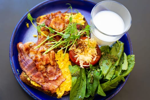 Very bright and healthy breakfast on a plate - bacon, egg, salad, tomato, cheese, a glass of yogurt. Close-up