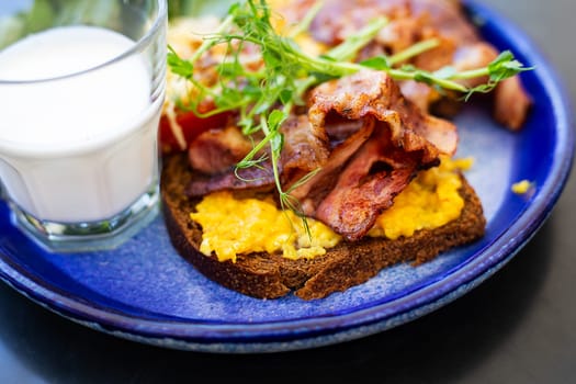 Very bright and healthy breakfast on a plate - bacon, egg, salad, tomato, cheese, a glass of yogurt. Close-up