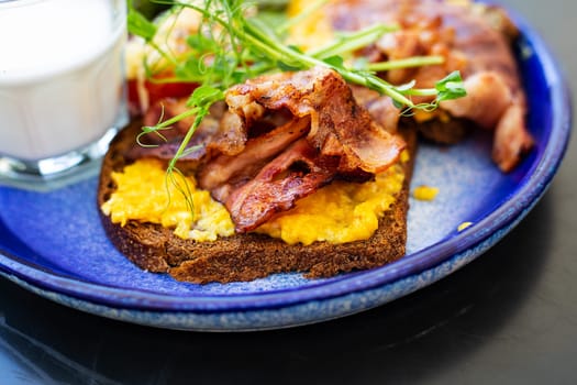 Very bright and healthy breakfast on a plate - bacon, egg, salad, tomato, cheese, a glass of yogurt. Close-up